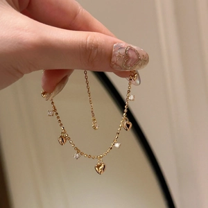 Dettaglio di un bracciale dorato con ciondoli a cuore e zirconi indossato al polso
