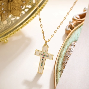 Detail of gold cross pendant with colorful zircons and white enamel on a fine chain