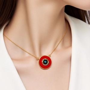 Close-up of a red evil eye necklace with gold chain and zircon detailing on a model