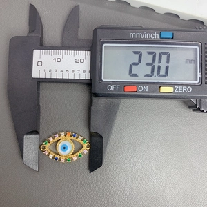 Macro shot of a 23mm golden evil eye pendant with multi-color stones on a digital caliper