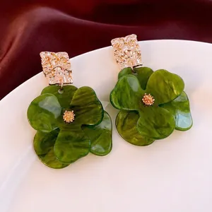 Retro acrylic flower earrings with green marble petals and gold accents on white porcelain