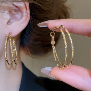 Detailed close-up of double-layered golden bamboo hoop earrings with textured finish