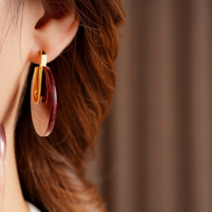 Close-up of a woman wearing gold-plated hoop earrings with amber acetate round pendants