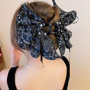 Detail of a large black paisley print bow hair claw clip with white pearls on a model