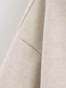 Detailed close-up showing texture of light beige wool fabric and fine stitching on jacket