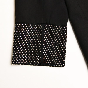 Dettaglio del polsino di un blazer nero decorato con strass lucidi su un tessuto liscio