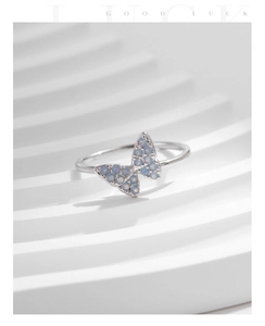 Detailed view of silver butterfly ring with light blue opal stones on wavy white background