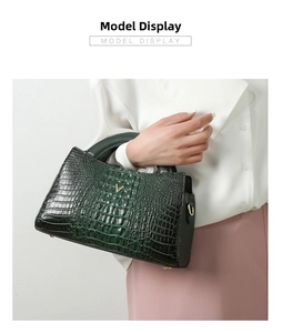 Detail of dark green crocodile pattern handbag with golden V logo held by a model