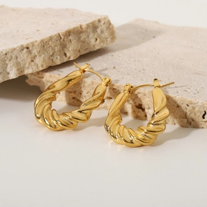 Detail showing gold-plated twisted hoop earrings on natural stone with polished finish