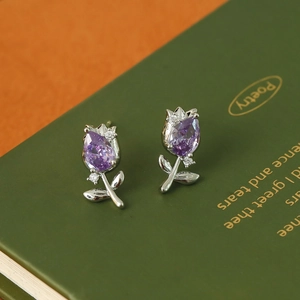 Macro shot of silver tulip stud earrings with purple zircon on a green book