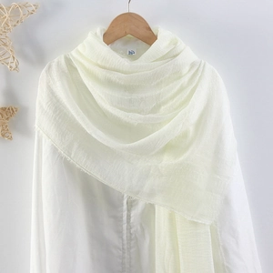Detail of white crinkled cotton linen scarf with soft texture hanging on a wooden hanger
