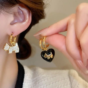 Detailed close-up of asymmetrical gold earrings featuring a rhinestone dog and black heart charm