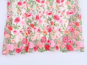 Gros plan d'une broderie florale complexe sur tulle avec des pétales rouges et roses