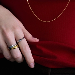 Primo piano di anelli ondulati oro e argento e collana sottile indossati da una modella