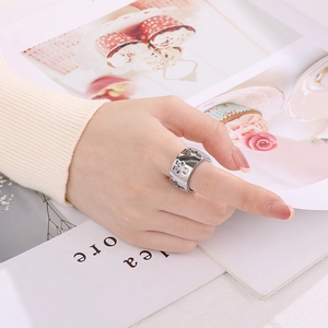 Detailed view of silver hollow cutout figures on a wide band stainless steel ring with rhinestones