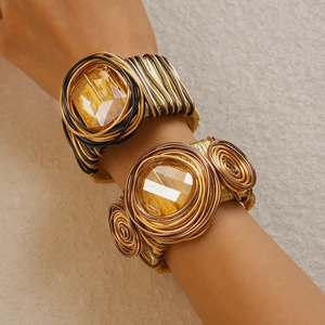 Detail of hand-woven wire cuffs with square and round yellow crystals on beige stone