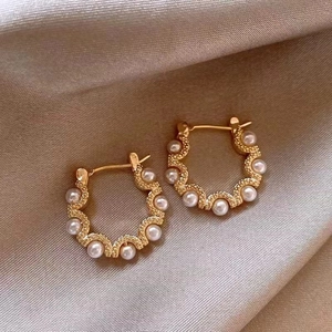 Close-up of golden wavy hoop earrings with inlaid white pearls on champagne silk fabric