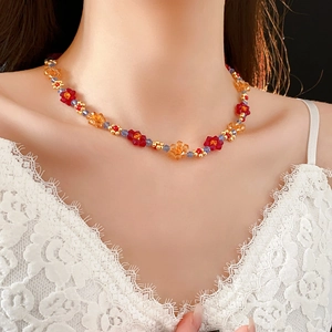 Gros plan d'un collier de fleurs en perles rouge et orange porté sur fond noir