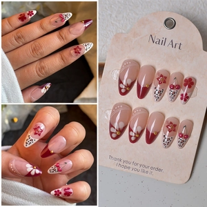 Macro view of long almond press-on nails with cherry, leopard print, and 3D gold studs
