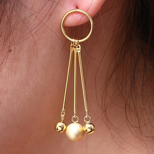 Detail of gold tassel earrings with long bars and pearls worn on an earlobe