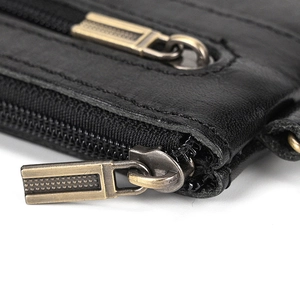 Detail of vintage black leather coin pouch with dual antique brass zippers and pebbled texture