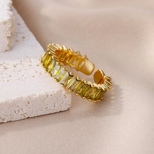 Detail of adjustable gold ring featuring baguette-cut yellow zircon stones on stone background