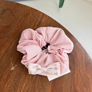 Detail of pink floral scrunchie with a cream bow on a rustic wooden table surface