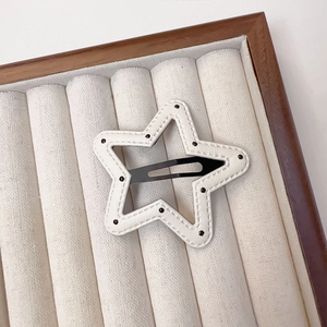 Macro detail of star-shaped white leather BB hair clip with black dots and stitching
