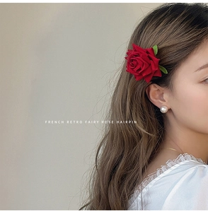 Close-up of a vintage red velvet rose hairpin with green leaf worn on a side bun hairstyle