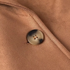 Close-up of a gradient round four-hole button on brown suede fabric coat detail