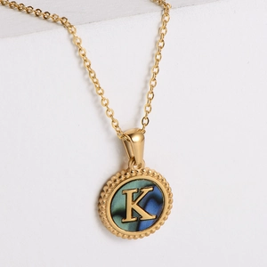 Detail of a gold letter K pendant with iridescent shell inlay and beaded edges