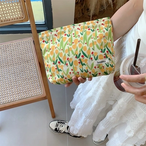 Detail of yellow canvas makeup bag with tulip print and logo tag in a lifestyle setting