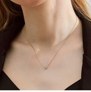 Close-up of sparkling six-prong zircon pendant on a gold bamboo chain worn by a model