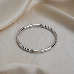 Polished silver stainless steel bangle displayed on elegant champagne satin fabric background