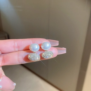 Close-up of pearl and rhinestone stud earrings with gold finish on a hand