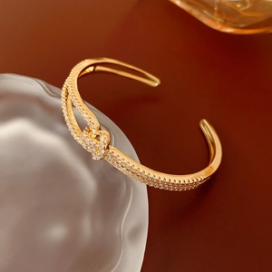 Detail of gold-plated knot bracelet featuring micro-paved zircons on a glass rim