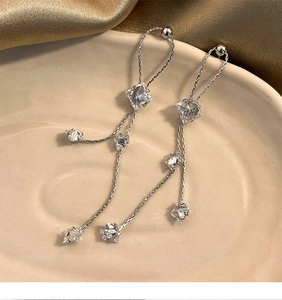 Macro shot of silver tassel earrings with zircon stones on a beige ceramic tray