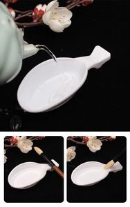 Macro shot of fish-shaped white ceramic brush rest and ink dish on dark background