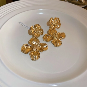 Close-up of golden metallic floral earrings with irregular 3D textured petals