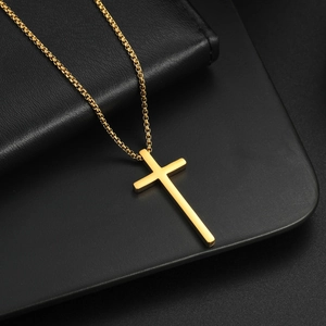 Macro shot of gold stainless steel cross pendant with box chain on black leather background