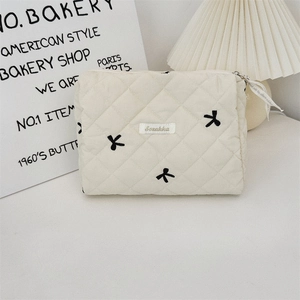 Close-up of beige quilted makeup bag with black bow embroidery and metal zipper detail