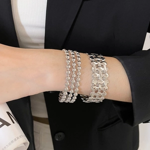 Detail of multi-layered silver geometric hollow cuff and bead chain bracelets on wrist