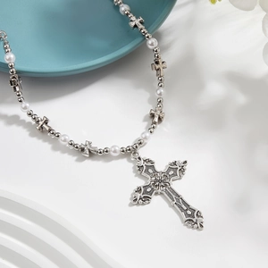 Retro cross pendant necklace with white pearls and silver metal chain on a white surface