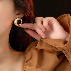 Close-up of vintage gold woven earrings with black resin inlay worn by a model