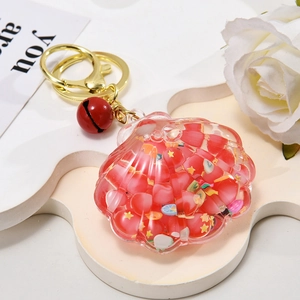Detailed view of seashell oil-filled keychain with red beads and golden bell charm