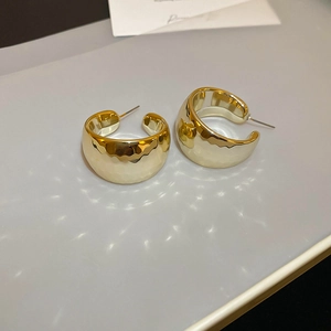 Close-up of golden wide C-shaped earrings with diamond pattern texture on grey background
