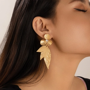 Macro detail of golden flower and ginkgo leaf earrings with pearl on a female model