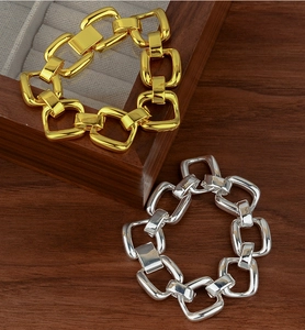 Detailed view of gold and silver chunky square link bracelets on a wooden jewelry stand