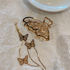Macro detail of golden butterfly hair claw clip with long tassel on white fabric
