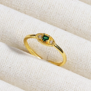 Detailed close-up of emerald and zircon gold ring on soft beige fabric background